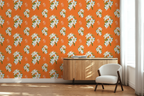 Bright room corner with bright Hermes orange wallpaper featuring a repeating white floral pattern with orange tigers, a light wood sideboard, and a white upholstered chair near a window.