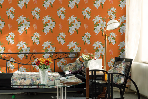 Bright bedroom scene featuring a Hermes orange wallpaper with large white floral prints, styled with a bed, chair, lamp, and floral accents.