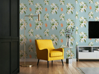 A styled living room corner featuring light Tiffany blue wallpaper with a white lily floral pattern with small tigers, a bright yellow armchair, a gold floor lamp, and a white sideboard with a TV mounted on the wall.