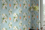 Tiffany blue wallpaper with a repeating pattern of white lilies, green leaves, and small orange tiger illustrations, shown installed on a wall in a room corner with a window and potted plants.