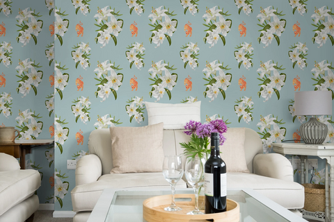 A styled living room featuring Tiffany blue wallpaper with a repeating white lily and orange tigers pattern, a cream sofa with beige cushions, a glass coffee table, and a bottle of red wine on a wooden tray.