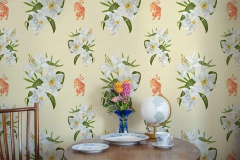 Small wooden table with porcelain tea cups, white plates, flowers, a globe, and a wallpaper with a pattern of white lilies and orange tigers. 
