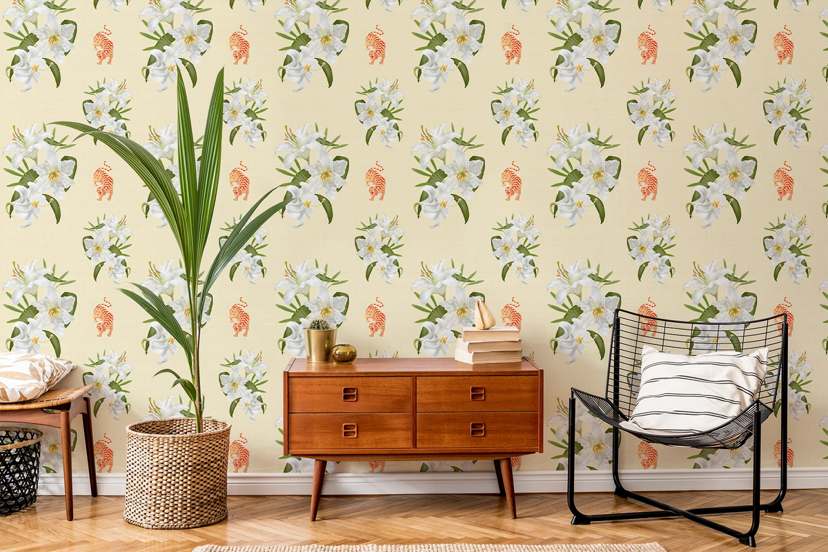 A styled interior room featuring wallpaper with a repeating pattern of white flowers, green leaves, and small orange tigers on a pale yellow background. A mid-century wooden sideboard, a black wire chair with a striped pillow, a tall potted plant, and a small table are arranged in front of the wall.