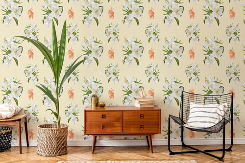 A styled interior room featuring wallpaper with a repeating pattern of white flowers, green leaves, and small orange tigers on a pale yellow background. A mid-century wooden sideboard, a black wire chair with a striped pillow, a tall potted plant, and a small table are arranged in front of the wall.