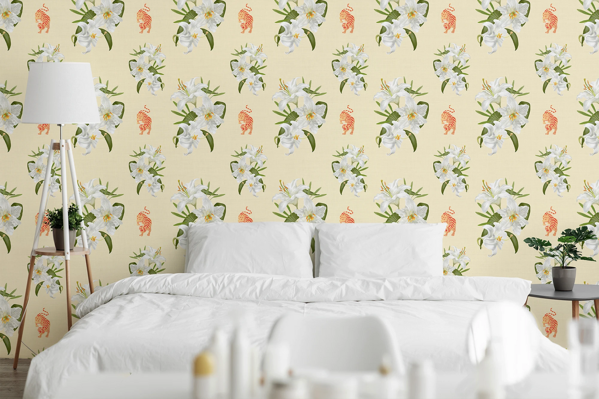 A styled bedroom scene featuring a bed with white bedding and pillows, set against a wall covered in a repeating floral wallpaper pattern with white flowers, green leaves, and small orange tigers on a pale yellow background.