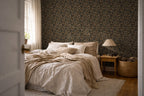 A modern bedroom with beige and white linens, a wooden nightstand, and the wall features a tapestry wallpaper with an oak leaf pattern. 
