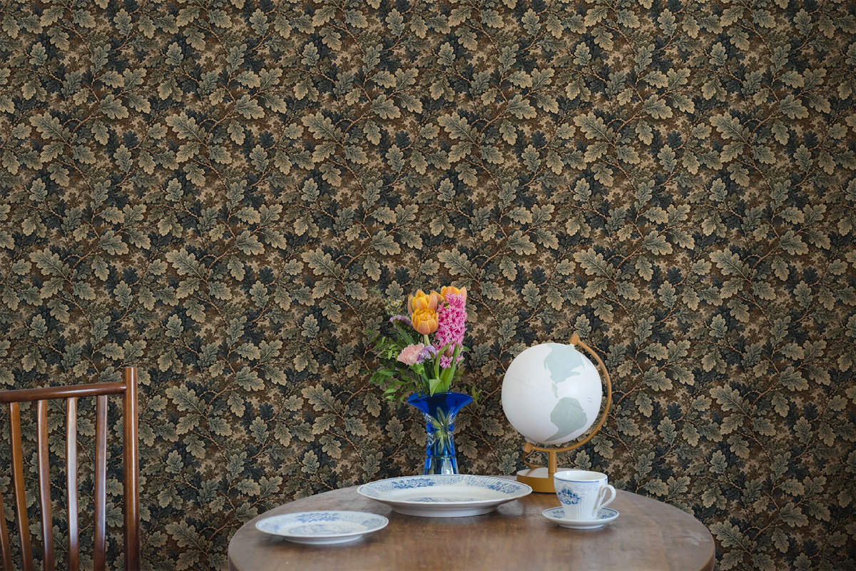 Small wooden kitchen table with a vase, a globe, two plates, and a cup. The wall behind the table as a beautiful tapestry wallpaper with an oak leaf pattern. 