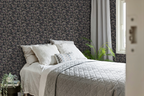 Modern bedroom with a grey and white bedcover, a plant, and a wall with a tapestry wallpaper featuring a dark oak leaf pattern. 