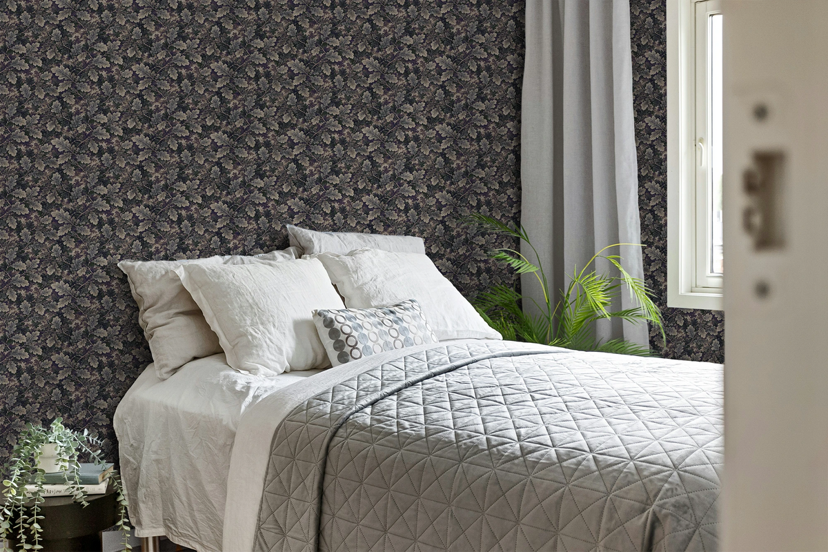 Modern bedroom with a grey and white bedcover, a plant, and a wall with a tapestry wallpaper featuring a dark oak leaf pattern. 