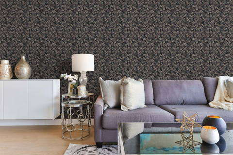 Modern living room with a blue sofa, a glass sofa table, and a wall with a tapestry wallpaper featuring a dark oak leaf pattern. 