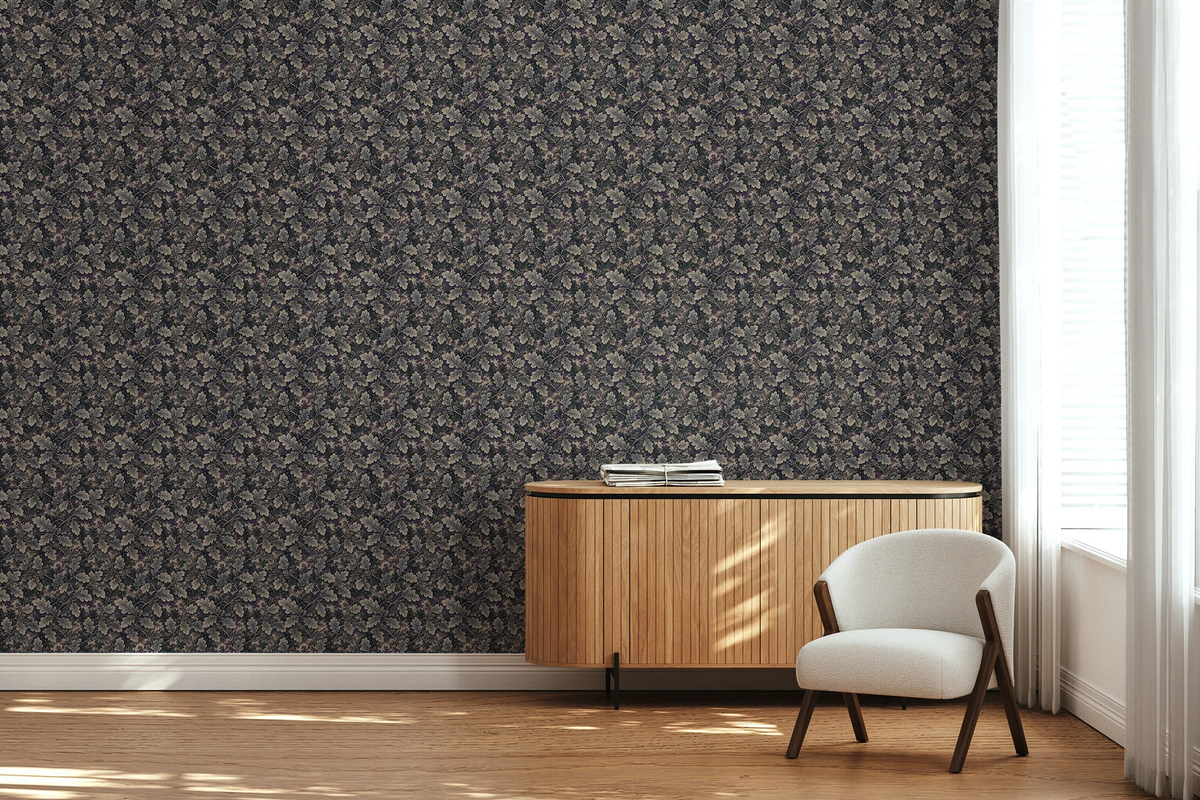 A modern lounge with a white textile chair, a wooden side board, and a tapestry wallpaper featuring a dark oak leaf pattern. 