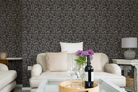 Modern living room with a white sofa, a glass sofa table, and a wall with a tapestry wallpaper featuring a dark oak leaf pattern. 