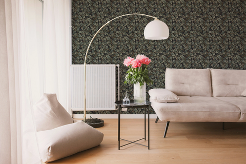 Modern living room with a white sofa, a glass sofa table, and a wall with a tapestry wallpaper featuring a green oak leaf pattern. 