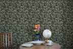 Kitchen table with a tea set, wooden table, a globe, a vase, and a wall with a tapestry wallpaper featuring a green oak leaf pattern. 