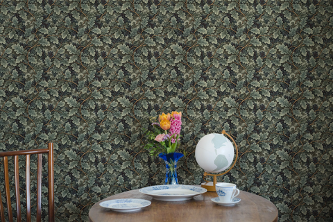Kitchen table with a tea set, wooden table, a globe, a vase, and a wall with a tapestry wallpaper featuring a green oak leaf pattern. 