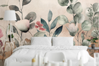 Pink and sage green floral bedroom wallpaper behind white bedding, styled with a wooden tripod lamp.
