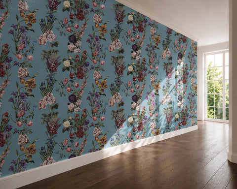 A room interior with a large wall covered in a dense floral wallpaper pattern on a dusty blue background. The wallpaper features multicolored flowers and foliage.