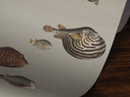A close-up of a textured light gray surface featuring detailed illustrations of various pufferfish in muted brown, gray, and gold tones, with a dark wood surface visible in the lower right corner.