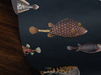 A close-up of a dark navy wallpaper featuring realistic pufferfish illustrations, shown partially rolled over a dark wood surface.